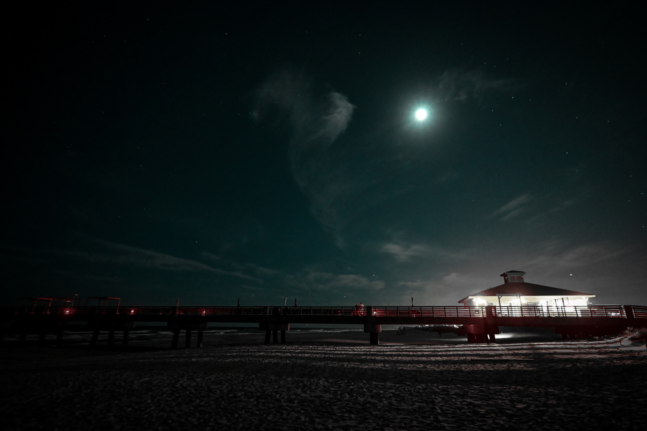 The Jacksonville Beach Pier under a moonlit cyan sky.