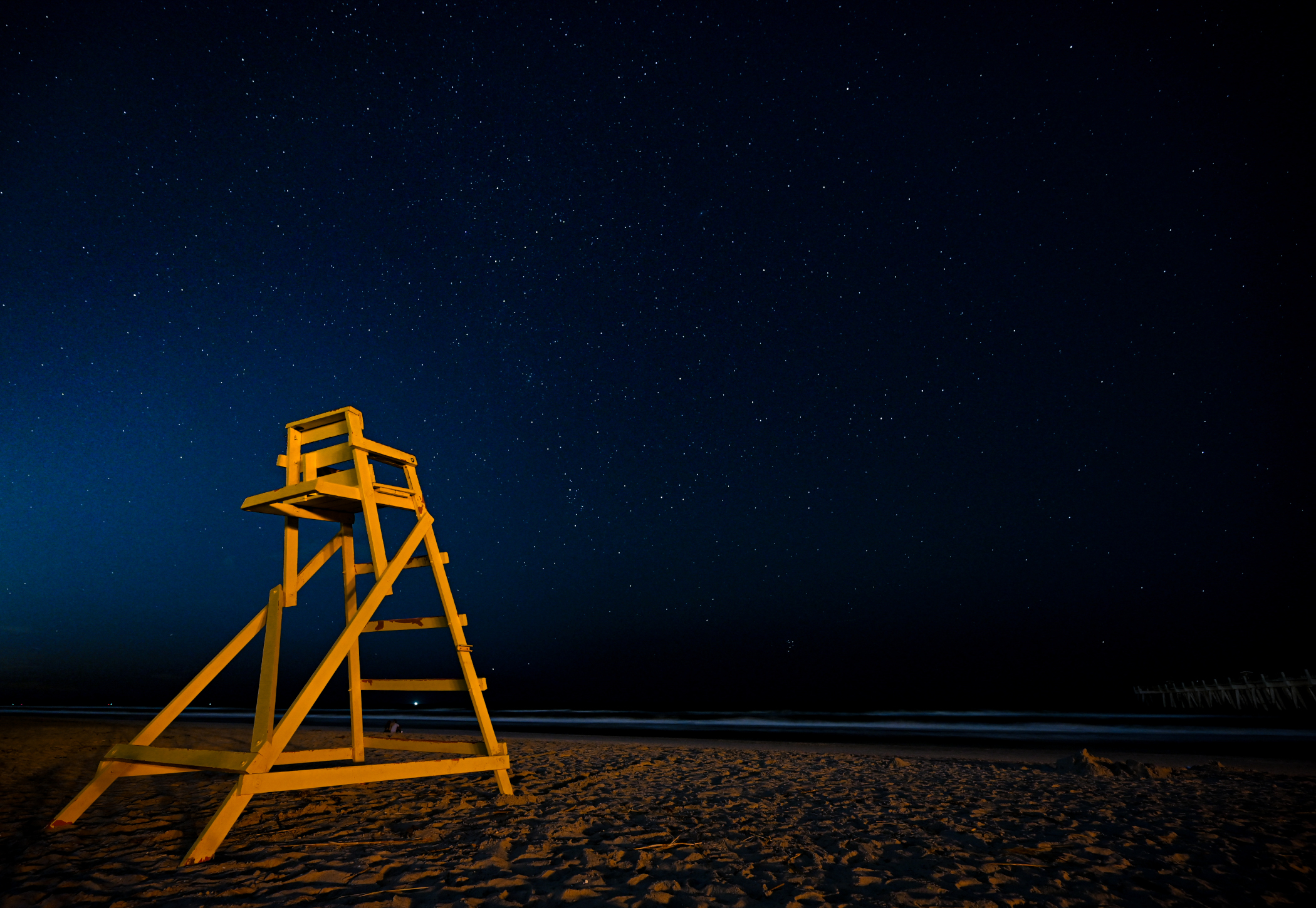 A yellow lifeguard chair under a clear starry sky on Jacksonville Beach Florida.