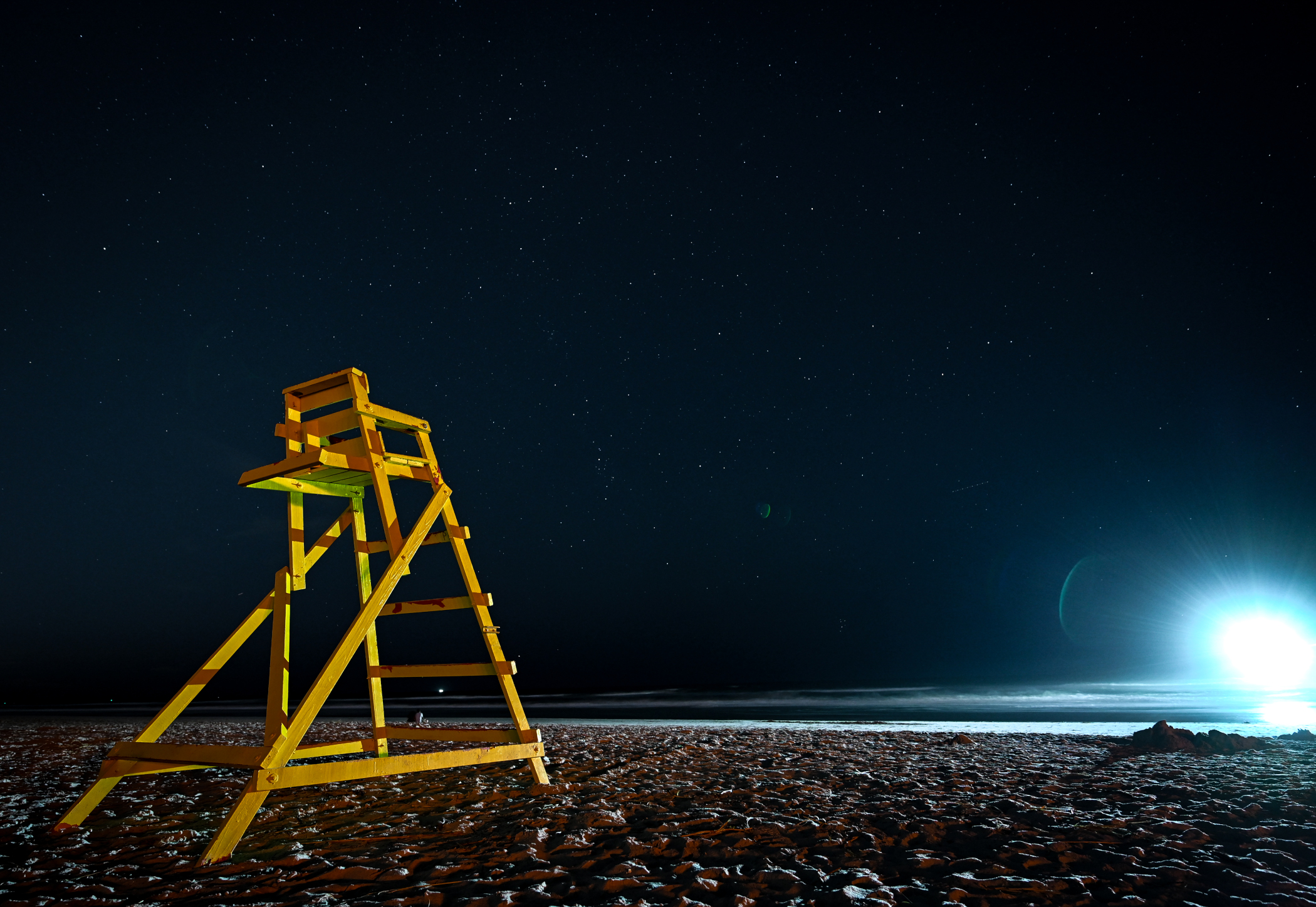 Bright slight from a boat that looks like an alien spacecraft with yellow lifeguard chair under a clear starry sky on Jacksonville Beach Florida.