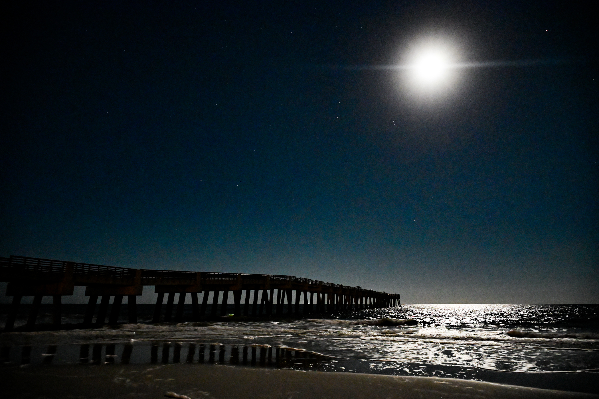 The Jacksonville Beach pier under a starry night with a deep cyan sky.