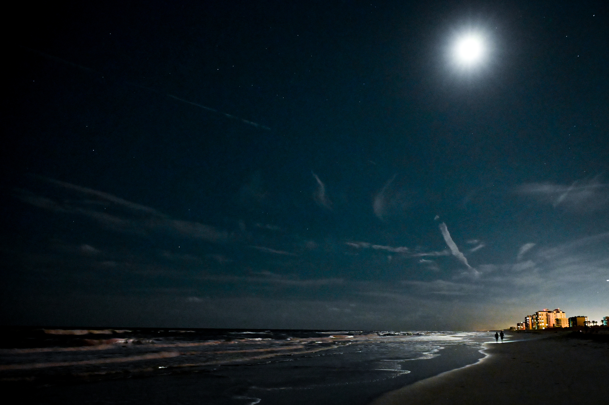 A dazzled moon over Jacksonville Beach Florida with deep cyan skies and wispy clouds.